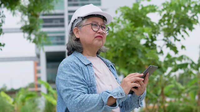Positive age Asian female architecture in hardhat hold tablet and standing in front of city for inspect building after construction complete, Engineering, construction concept.