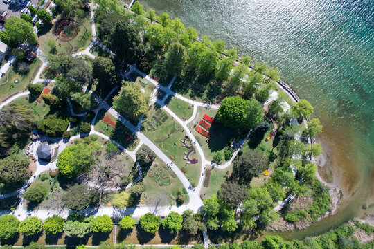 Aerial view of Parc de l'Independance with vibrant flower beds, winding paths, and lush green trees along the shores of Lake Geneva in Morges, Vaud, Switzerland.