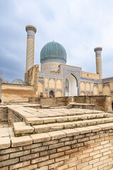 Obraz premium Gur-e-Amir Mausoleum with its turquoise dome and minarets, framed by historic brick ruins, Samarkand. Hidden layers and foundations of historic sites.