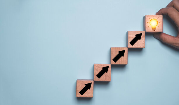 Idea development to business growth concept with rising arrow blocks and glowing light bulb, symbolizing innovation, creative strategy, progress improvement, leadership and success planning