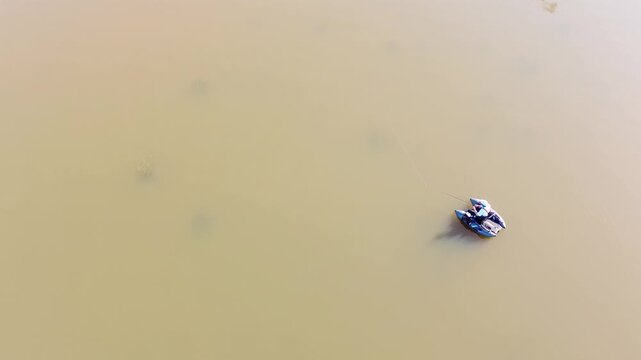 Aerial top down view of a fisherman in a sit-on-top kayak catching a fish in a calm lake