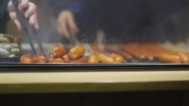 Bavarian Christmas market, sausages sizzle on hot grill as vendor prepares quick street food. Steam rises, warm snacks are served, and festive winter setting highlights traditional German cuisine.