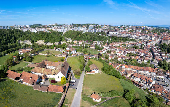 Aerial view of the historic Maigrauge Abbey and old town rooftops surrounded by lush greenery and modern urban architecture under a clear blue sky Fribourg, Fribourg, Switzerland.