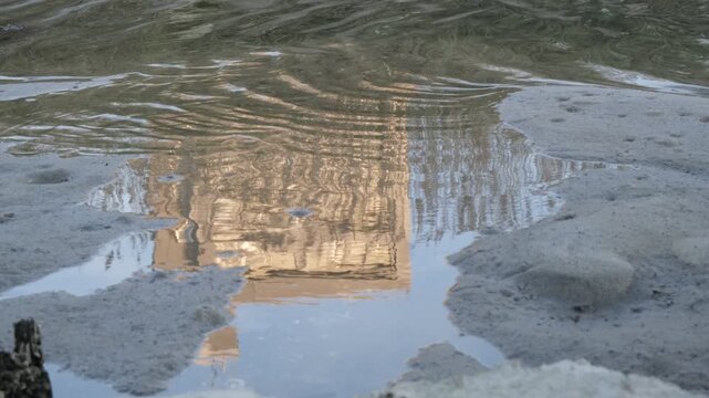 Silent puddle reflection of building and reeds with wind ripples, abstract riverside footage