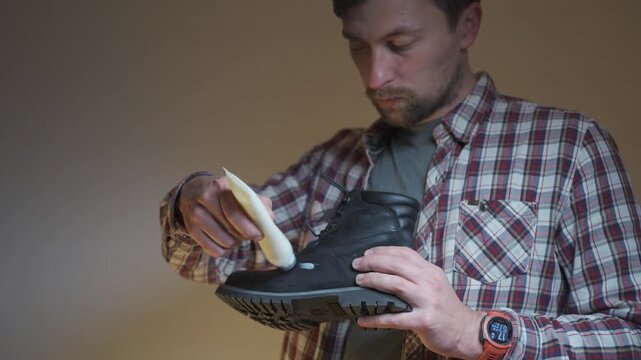 A man applies leather cream to a black boot, showing detailed shoe care and maintenance. The closeup highlights cleaning, conditioning and restoring footwear for long lasting protection.