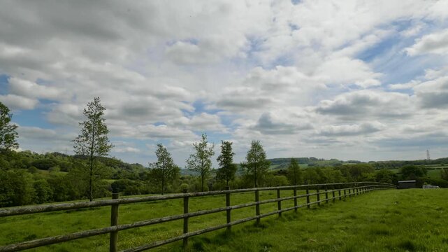 English countryside and farming picture showing a green field with a wooden fence acting as a strong leading line. A cloudy sky adds drama to the rural lifestyle image.