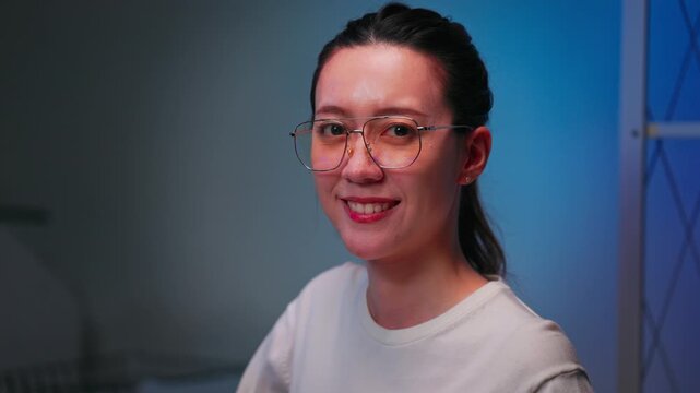 Asian woman working as software engineer in modern office at night before looking at camera with confident smile. Professional programmer, women in tech and career success concept.