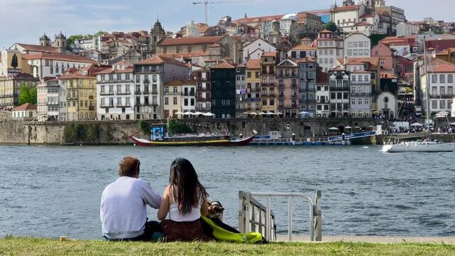 Pareja enamorada y su perro sentados junto al r&iacute;o Duero en Oporto con vistas panor&aacute;micas de la ciudad