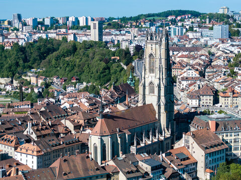 Aerial view of St-Nicolas Cathedral with its gothic tower rising above the historic rooftops and lush green hills in Fribourg, Fribourg, Switzerland.