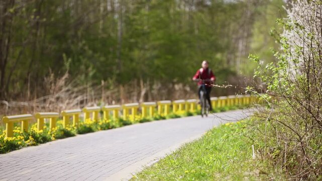 Young woman cycling on paved path along yellow railing in lush green park