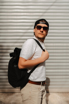 Man Carrying Backpack Against Shutter Looks Over Shoulder With Sunglasses, Textured Metal Background And Warm