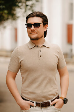 Man In Sunglasses Beige Polo Stands Relaxed With Hands In Pockets On Sunlit City Sidewalk, Warm Tones And Soft