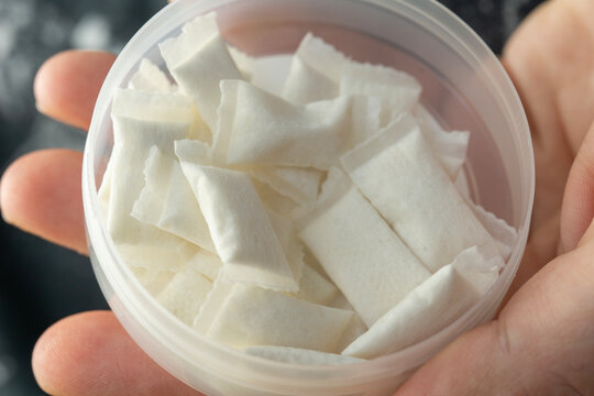 top view of open container with white nicotine pouches or snus portions in hand concept of smokeless tobacco, addiction risk, nicotine delivery habit and health danger