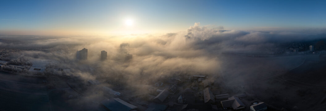 Aerial view of high-rise buildings and residential rooftops emerging from thick morning fog under a bright sun in Tubingen, Baden-Wurttemberg, Germany.