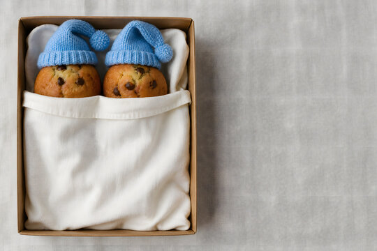 Muffins wearing tiny sleeping caps tucked into a paper bed from above
