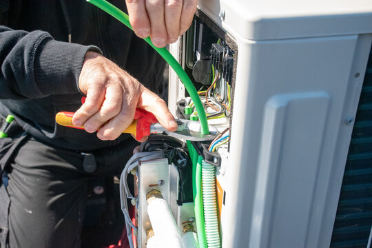 Technician Installing Modern Outdoor Air Conditioning Unit,Technician Working on an Air Source Heat Pump System,Close-up of Handyman Fixing Electrical Wiring in Outdoor Device