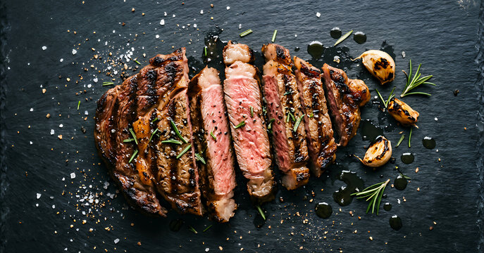 A beautifully cooked steak, sliced and garnished with herbs, garlic, and sea salt on a dark slate plate, showcasing its juicy and tender interior.