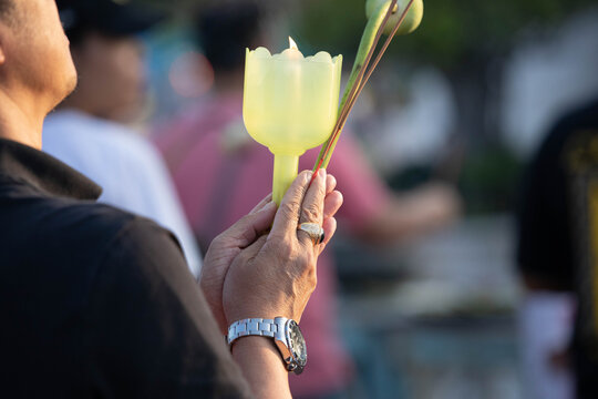 Senior male hands holding candlestick and lotus flower in candlelight procession around Buddha statue on Makha Bucha Day, close up.