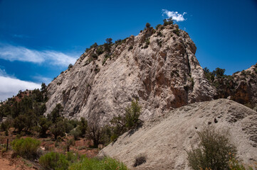 Fototapeta premium Rugged desert mountain cliffs under a vivid blue sky, with rocky slopes, sparse brush, and dramatic sunlit textures.