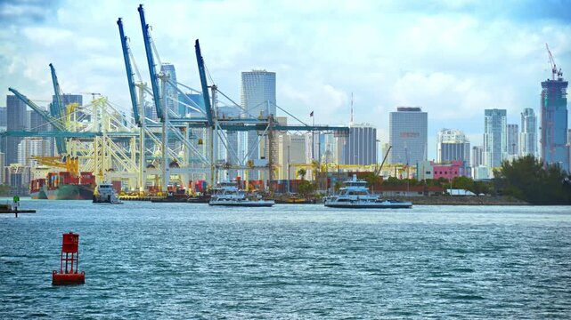 Motor boats move by the water near the large port. Huge ship loaded with containers stands at the docks. Miami Beach, Florida, USA.