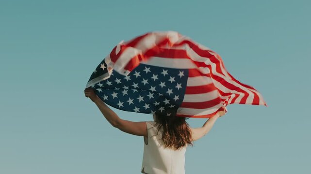 Lady Lifting Flag With Breeze. Woman Celebrating With American Flag Soaring High In Bright Air