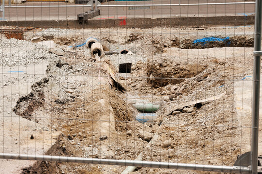 Construction site with gravel piles and safety barriers behind a wire fence. A view of an active construction site featuring piles of gravel, temporary barriers, and unfinished building structures