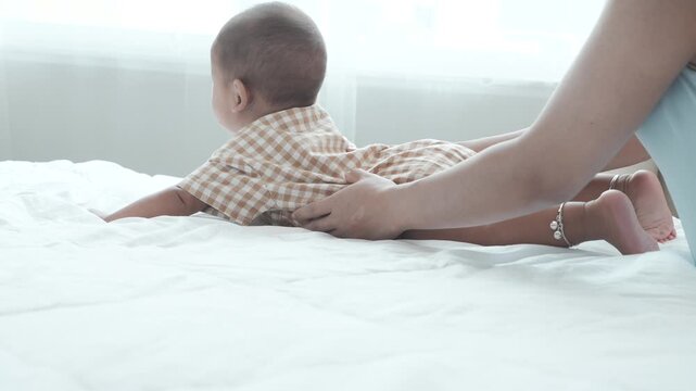 The seven-month-old baby is getting dressed for bed on the mattress at home.