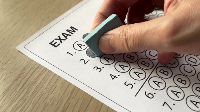 Hand erasing wrong answer on multiple choice exam sheet. Concept of correction, testing, mistake fixing, and academic evaluation