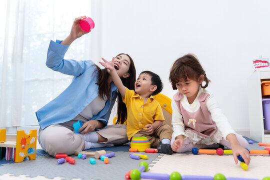 Asian teacher and diverse children playing with colorful educational toys in a bright nursery room