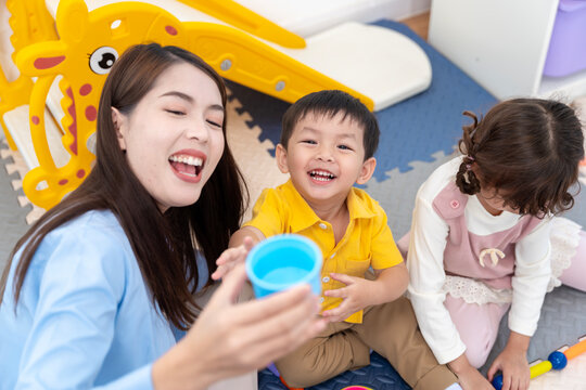 Asian teacher and diverse children playing with colorful educational toys in a bright nursery room