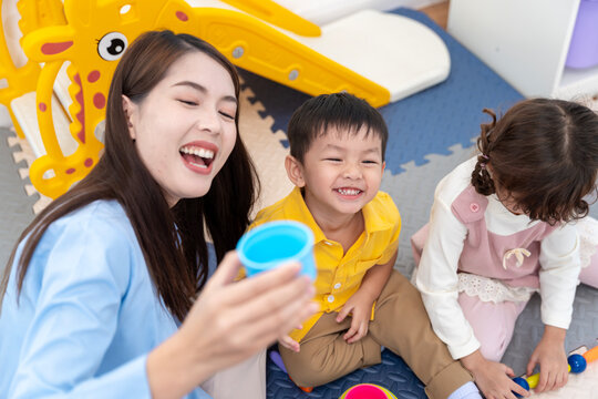 Asian teacher and diverse children playing with colorful educational toys in a bright nursery room