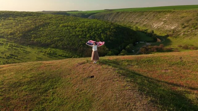 Wide Shot White Woman Waving Flag On Ridge At Sunset, Windblown Cape Over Valley, Emotive Patriotic Moment