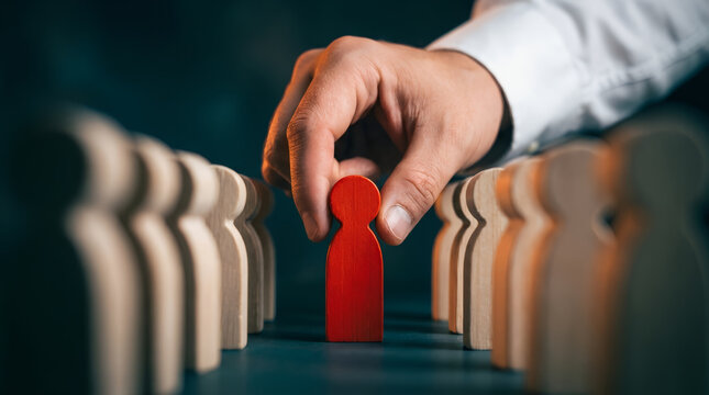 Man hand picking red wooden figure from row of plain ones. Concept of leadership, human resource management, talent acquisition and business recruitment. Unique individual selection.