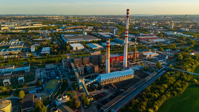 Aerial view of Malesice heating plant with tall striped chimneys and industrial buildings surrounded by green fields and urban roads during sunset Hlavni mesto Praha, Hlavni mesto Praha, Czechia.