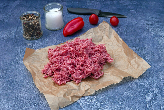 Frisches Rinderhackfleisch auf Pergamentpapier mit Messer und Gew&uuml;rzen auf einem Steinhintergrund.