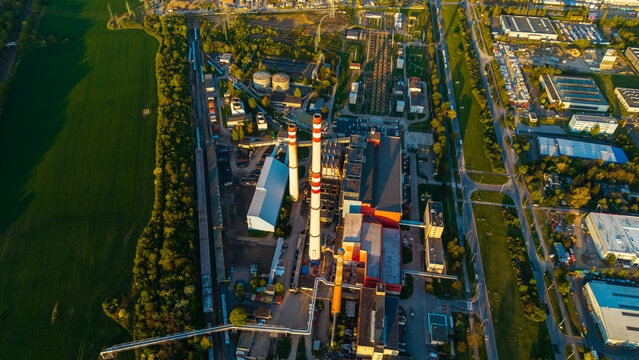 Aerial view of Malesice heating plant with tall striped chimneys and industrial buildings surrounded by green fields and urban roads during sunset Hlavni mesto Praha, Hlavni mesto Praha, Czechia.