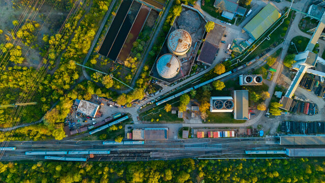 Aerial view of Malesice Infrastructure Objects featuring industrial silos, railway tracks with blue trains, and lush green trees in Hlavni mesto Praha, Hlavni mesto Praha, Czechia.