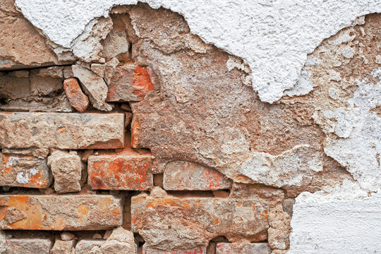 Old brick wall with peeling plaster and rough texture showing age in a building