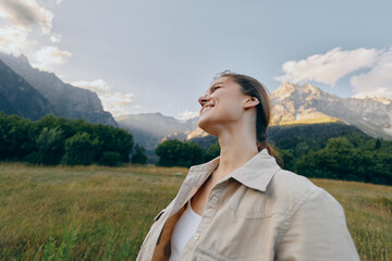 Naklejka premium Vibrant outdoor portrait of a woman in a field enjoying nature and mountain views, a carefree mood and smiling expression, capturing lifestyle in a serene moment