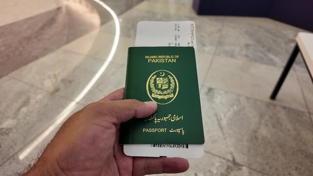 A man sits patiently at the airport, holding his Pakistan passport, waiting for his flight to begin his journey.