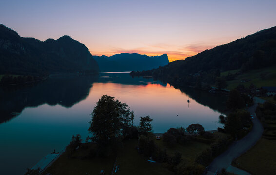 Sunset over Lake Mondsee in Austria with Drachenstein peak in the background, calm summer evening with reflections and alpine scenery.
