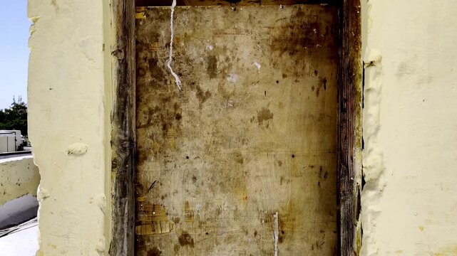Old damaged wooden door on rooftop terrace, weathered rustic wood with peeling paint showing abandoned building architecture and decay