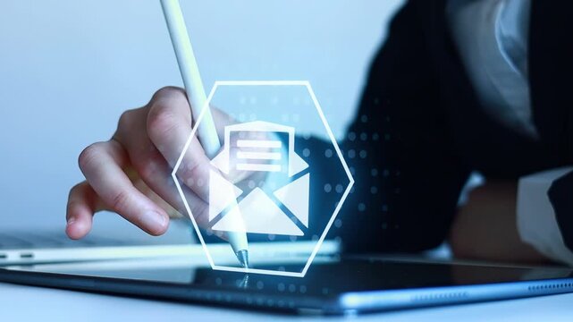 Person writes on tablet while looking at email icon in office setting during daytime.