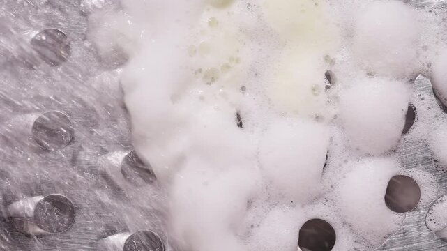 Thick Soap Foam Covering Metal Grater Surface with Water Flow, Macro Top View with Bubbles and Texture, Slow Motion Deep Cleaning Concept and Hygiene