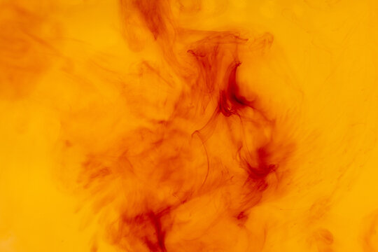Abstract red ink dissolving in warm yellow liquid background with soft flowing organic shapes