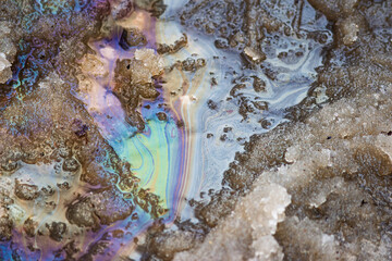 Naklejka premium Iridescent oil slick on wet spring snow, showing colorful patterns from petroleum contamination in melting ice and water