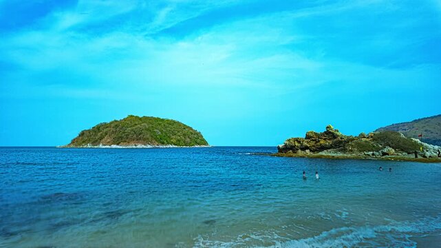 
Blue sky over a small island surrounded by blue sea. White beach dotted with coconut trees. Yanui Beach, a viewpoint next to Promthep Cape and windmills, is a small beach with a split sea.