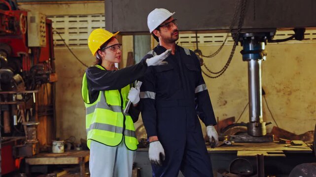 Industrial worker factory safety helmet high visibility vest protective eyewear machinery engineer inspection maintenance workshop, two workers coordinate drill press inspection with clipboard near