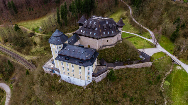 Aerial view of Klaus Castle, a historic fortress complex with stone walls and dark roofs nestled on a wooded hill near a railway line in Klaus an der Pyhrnbahn, Upper Austria, Austria.