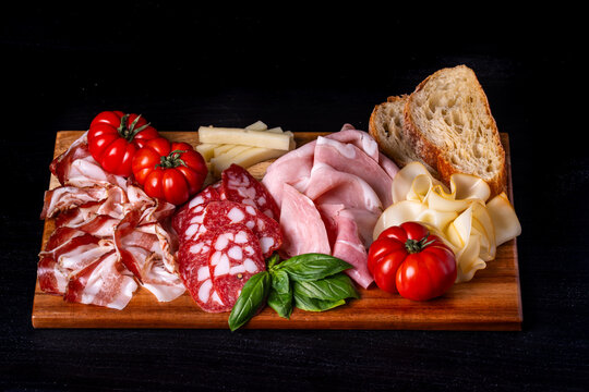 Tagliere all'italiana con prosciutto cotto arrosto, salame corallina, guanciale, pecorino stagionato, pomodori, pane e provola affumicata su sfondo scuro
